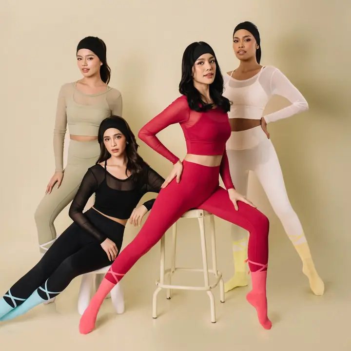 Five women in Reset mesh tops and leggings in sage, black, red and white, posed around a studio stool
